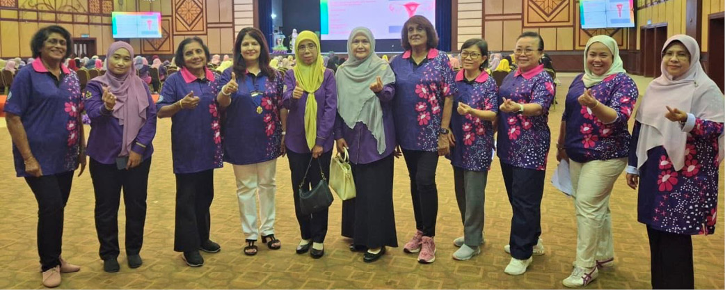 A group of adults wearing matching purple shirts with floral patterns stand together in a decorated indoor event space with chandeliers and large screens in the background.

Description generated by AI