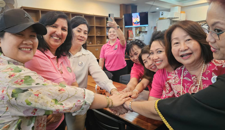 A group of people smiling and standing around a table with their hands stacked together in a gesture of unity in a well-lit room.

Description generated by AI