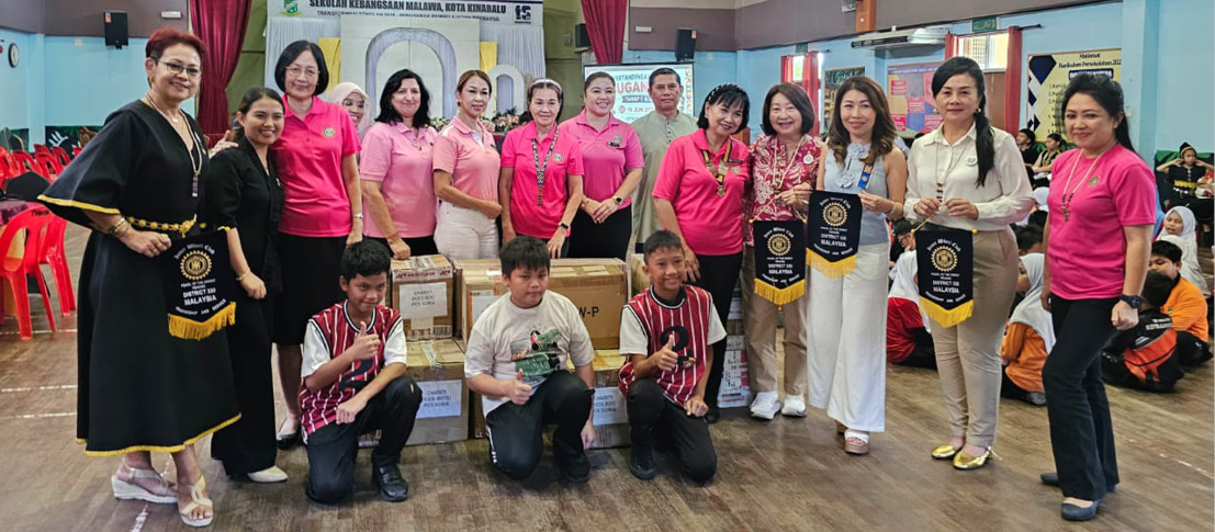 A group of adults wearing pink and casual clothing pose indoors around boxes and banners in a community or event setting.

Description generated by AI
