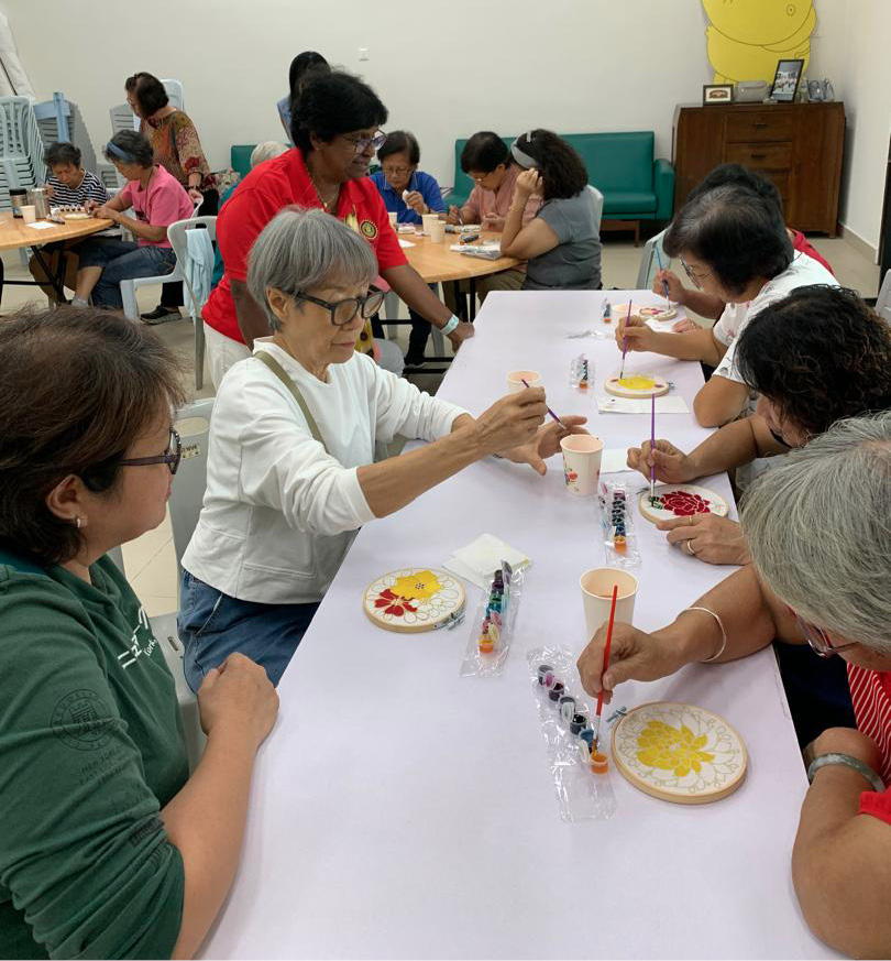A group of adults and seniors are seated around tables engaged in painting colorful designs on plates in a well-lit room.
Description generated by AI