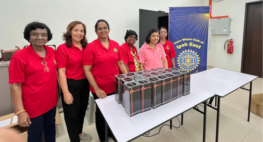 Six adults wearing red and pink shirts stand behind a table with neatly arranged gift boxes in a bright room with a banner in the background.
Description generated by AI