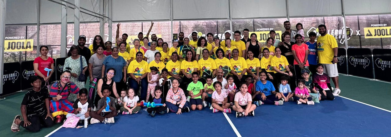 A large group of people, including many wearing yellow shirts, are gathered and posing together on an indoor sports court under a tent-like structure.
Description generated by AI
