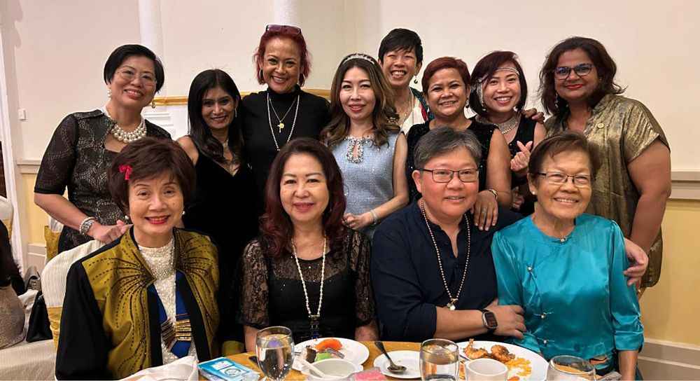 A group of people smiling and posing together around a table with plates and glasses in a warmly lit indoor setting.
Description generated by AI
