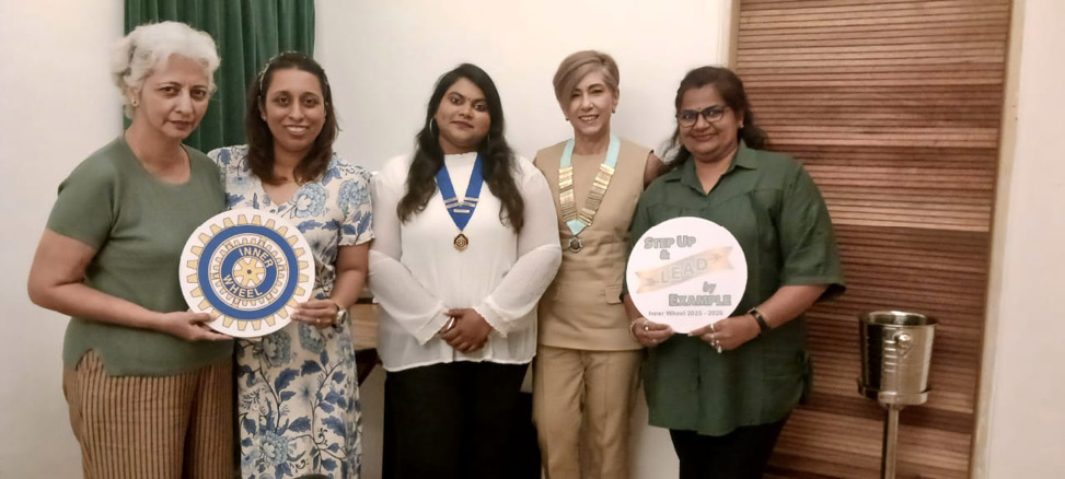 Five adults stand indoors holding two circular plaques, with one person wearing a medal and another wearing a chain of office, all smiling and dressed in casual to semi-formal attire.
Description generated by AI